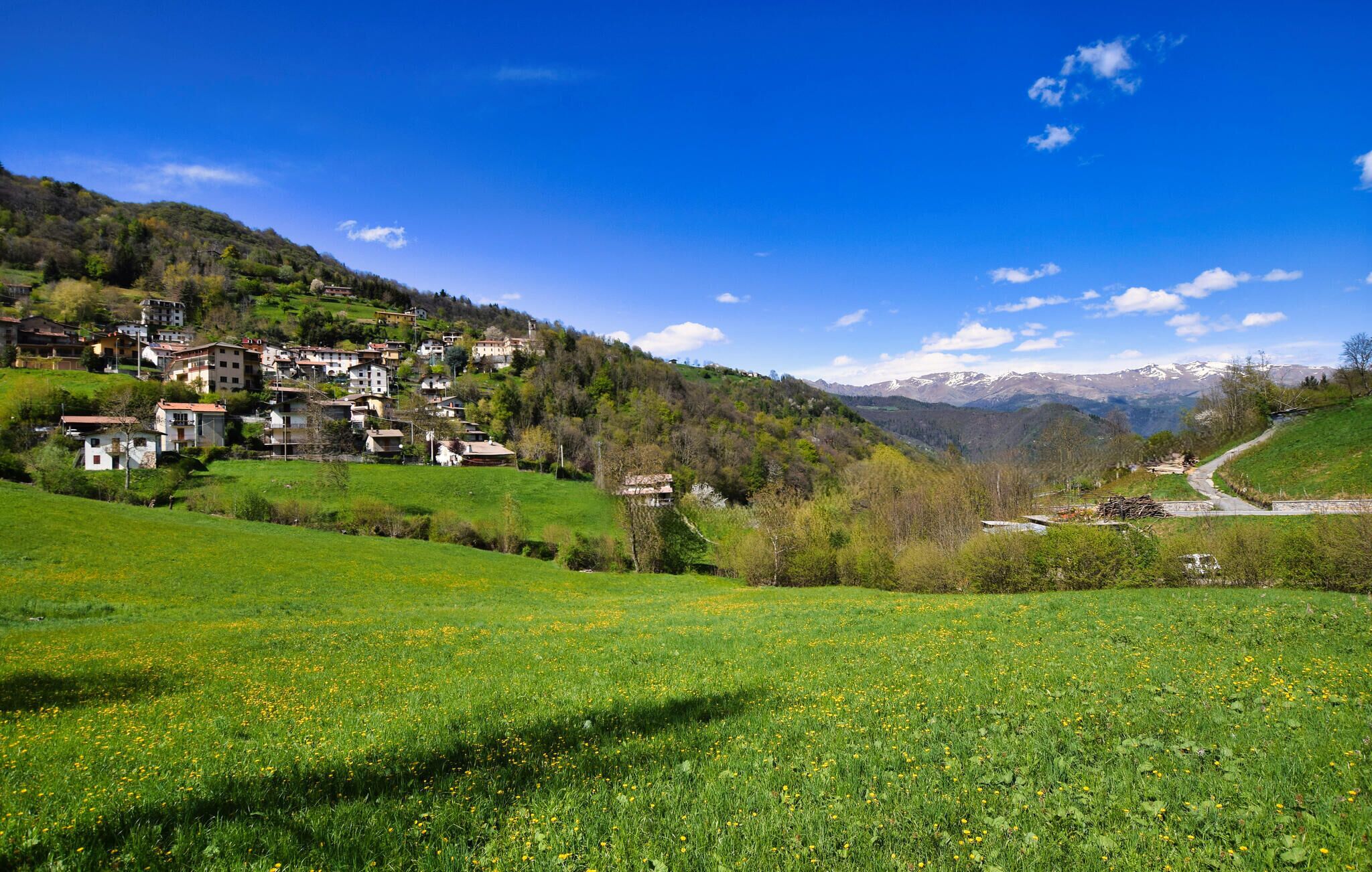 A hillside village with traditional buildings, a clear sky, and a valley with mountains in the background.