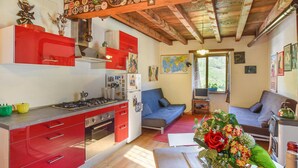 Eine kompakte Küche mit roten Schränken, einem Gasherd und einem Kühlschrank. Es gibt ein blaues Sofa und einen kleinen Tisch mit einer Zierpflanze.