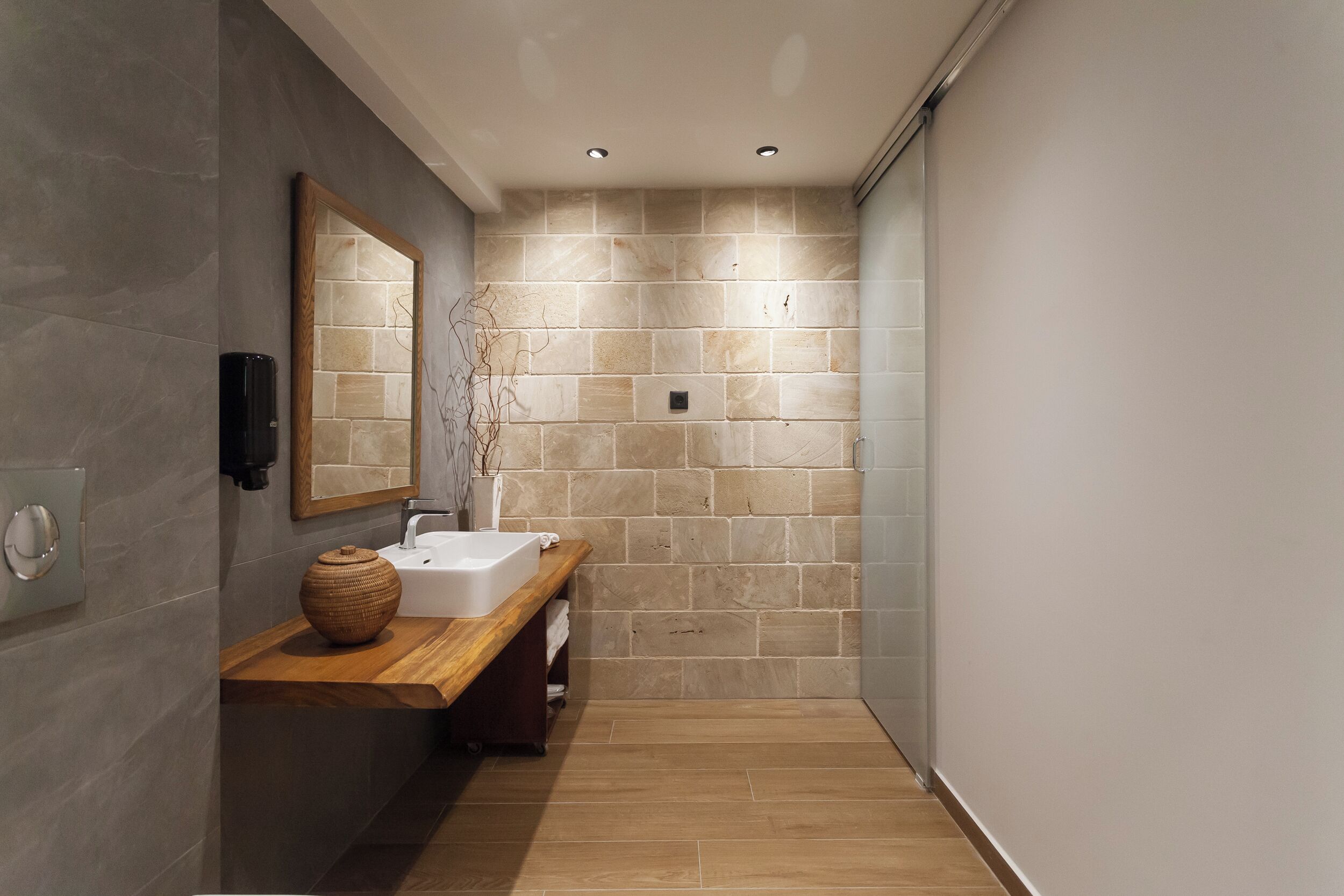 A modern bathroom with a wooden vanity, a large mirror, and a tiled wall.