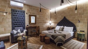 Un dormitorio moderno con una cama grande, una zona de estar con un sillón acolchado, un escritorio pequeño y un aire acondicionado de pared.