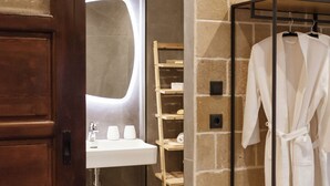 Un baño con puerta de madera, un lavamanos blanco, un espejo y un perchero para bata.
