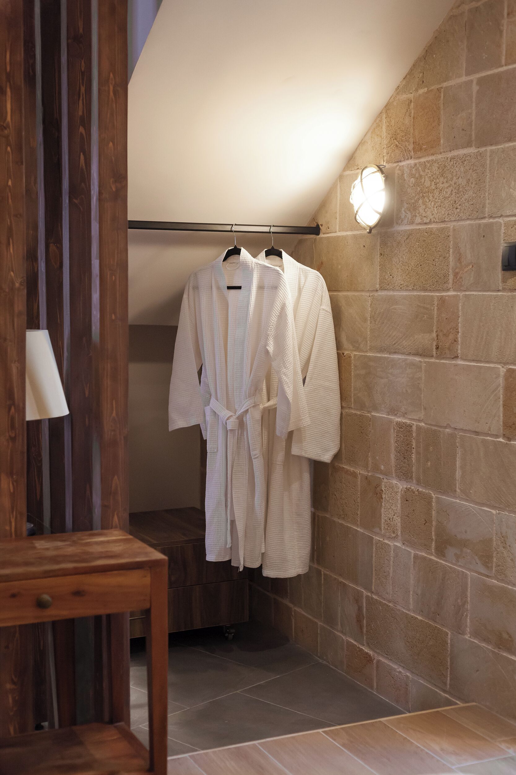 Un baño con tocador de madera, una bata colgada en un perchero y una pared de piedra.