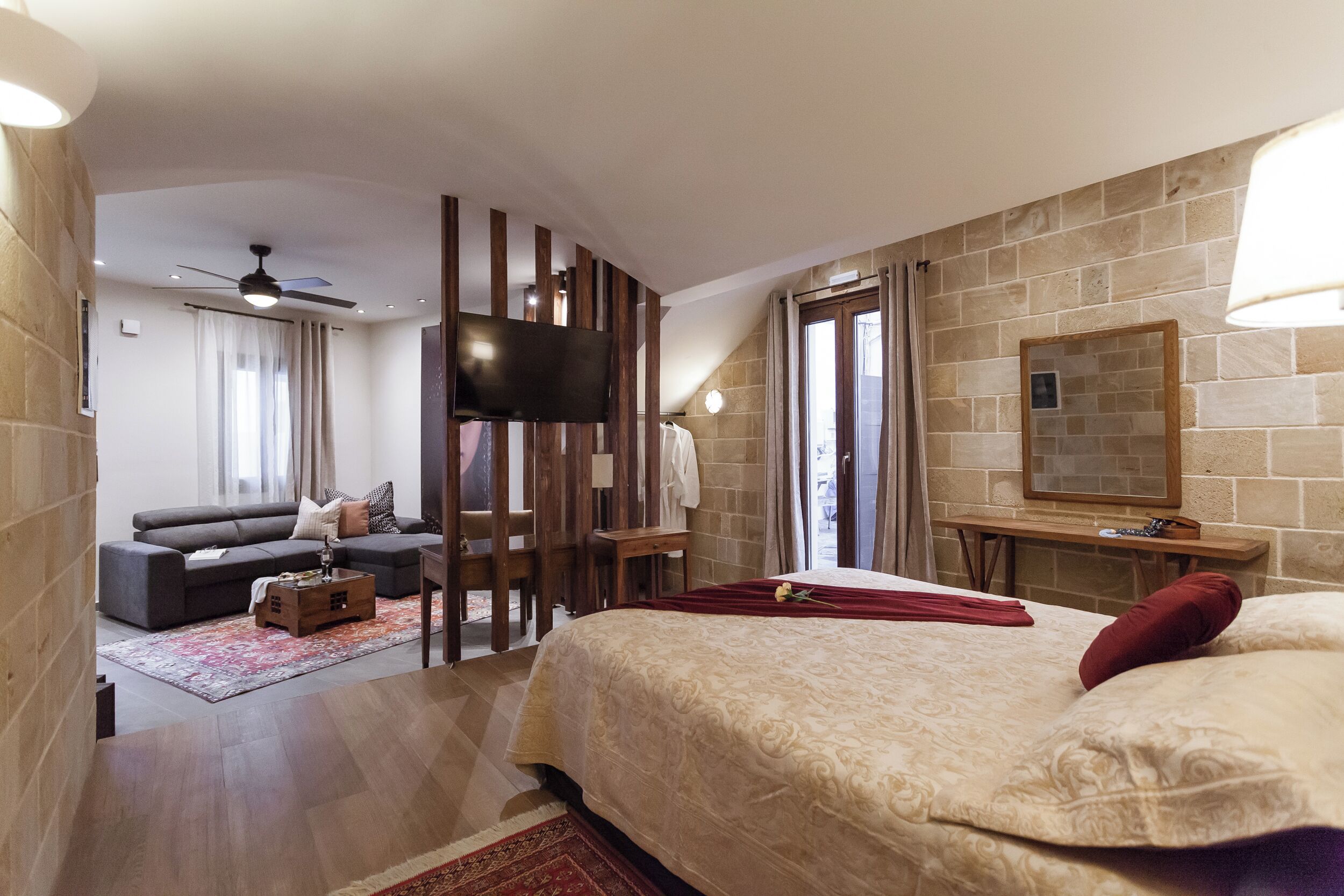 A modern hotel room with a large bed, a TV mounted on the wall, a sofa, and a small table.