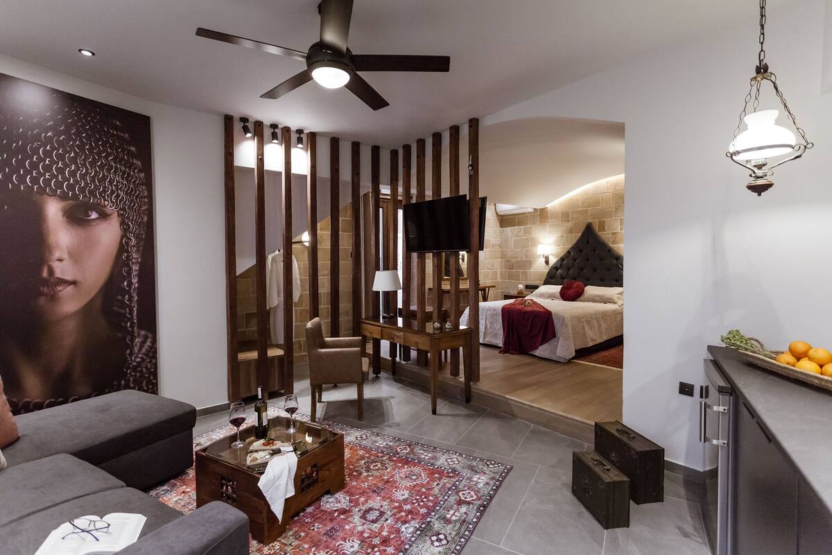 Una sala moderna con un sofá, una mesa de centro y un televisor. Una escalera conduce a un dormitorio con una cama y un televisor.