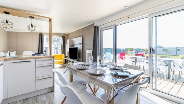 A modern kitchen with white cabinets, a wooden countertop, and a dining area with a glass table and chairs. - Holiday at 6 in a résidence with heated pool (Bretignolles-sur-Mer)