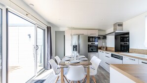A modern kitchen with white cabinets, a wooden countertop, and a dining area with a glass table and white chairs. - Holiday at 6 in a résidence with heated pool (Bretignolles-sur-Mer)