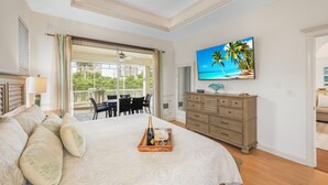 Un dormitorio con cama, cómoda, televisor en la pared y balcón con mobiliario exterior.