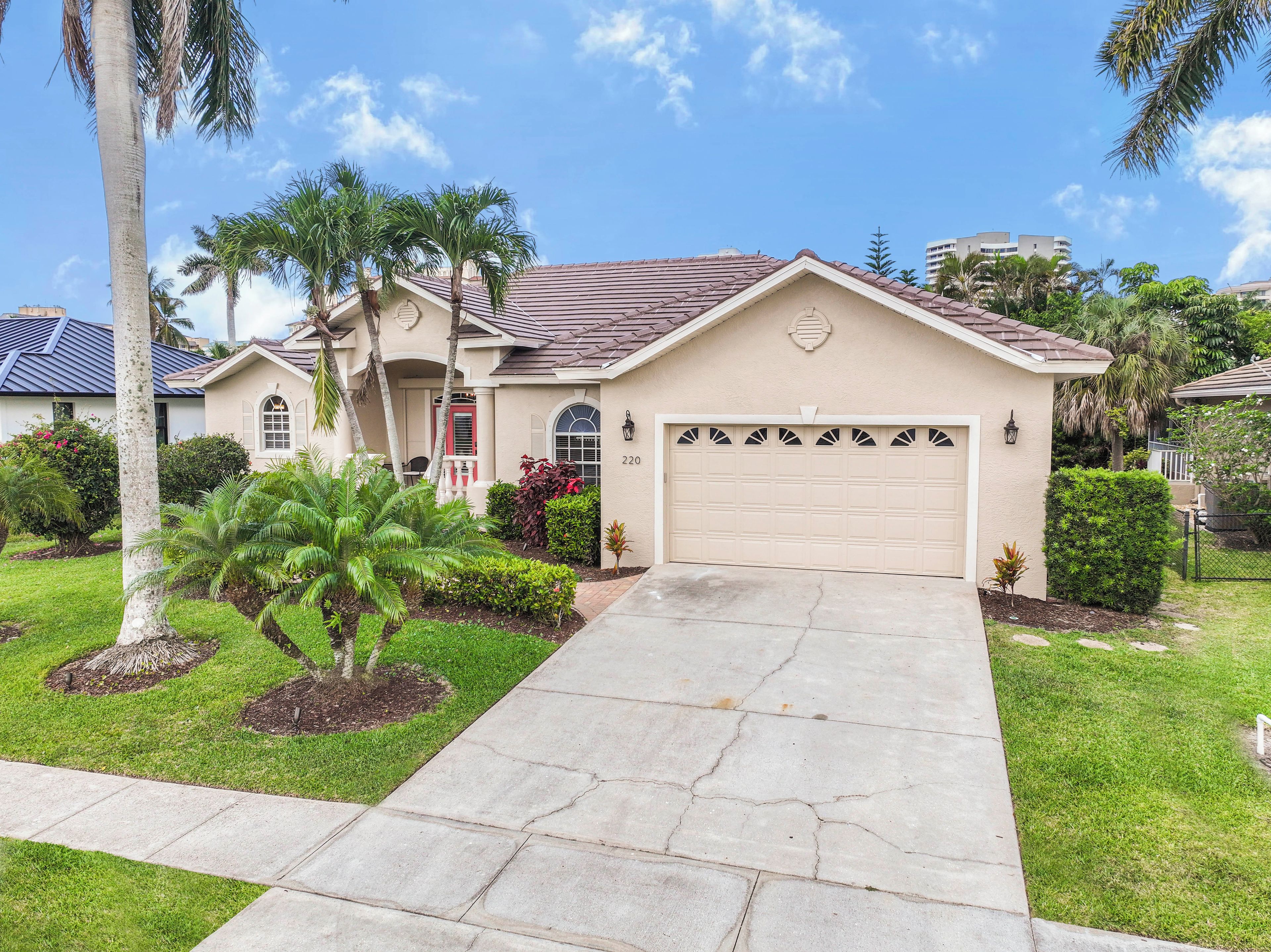 A residential house with a garage, a driveway, and a well-maintained lawn with palm trees.