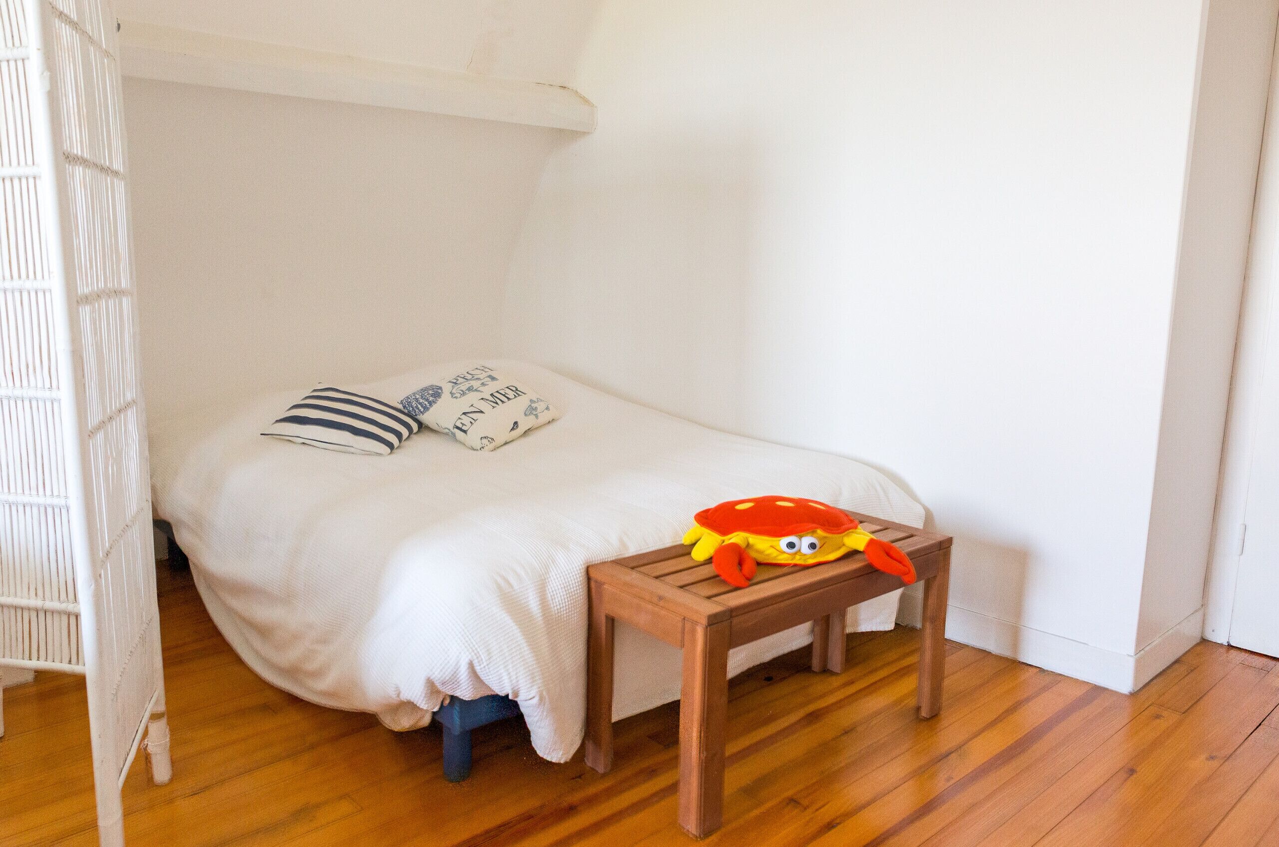 Une petite pièce, bien aménagée, avec un lit simple, une table de chevet en bois et un berceau blanc.