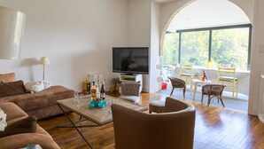 Een ruime woonkamer met een flatscreen-tv, comfortabele zithoek en een groot raam met uitzicht op groen.