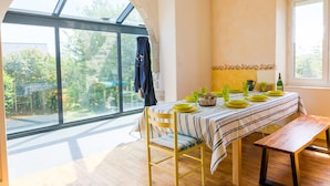 Een eetruimte met een tafel voor vier personen, grote ramen en uitzicht op groen.