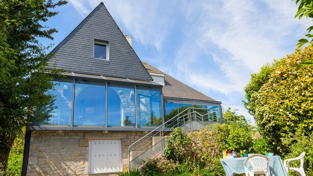 Een modern huis met een gevel van natuursteen, grote ramen en een trap die naar een terras leidt.