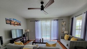 Una sala de estar con un sofá gris, una televisión y un ventilador de techo.