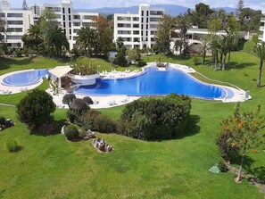 A large, oval-shaped swimming pool with a surrounding deck, surrounded by well-maintained lawns and trees.