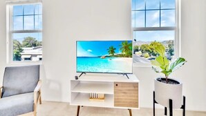 Un soggiorno moderno con una TV a schermo piatto su un mobile bianco, una poltrona grigia e una pianta in vaso.
