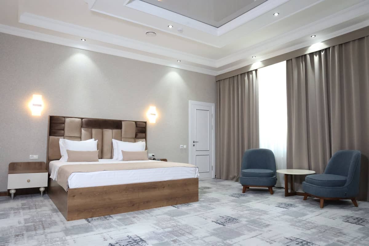 A hotel room with a large bed, two nightstands, a round table, two chairs, and a door.