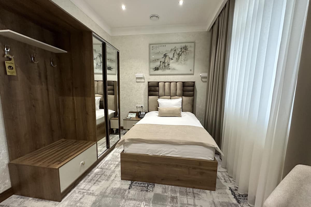 A modern hotel room with a large bed, a wooden bench, a wardrobe, and a mirror.