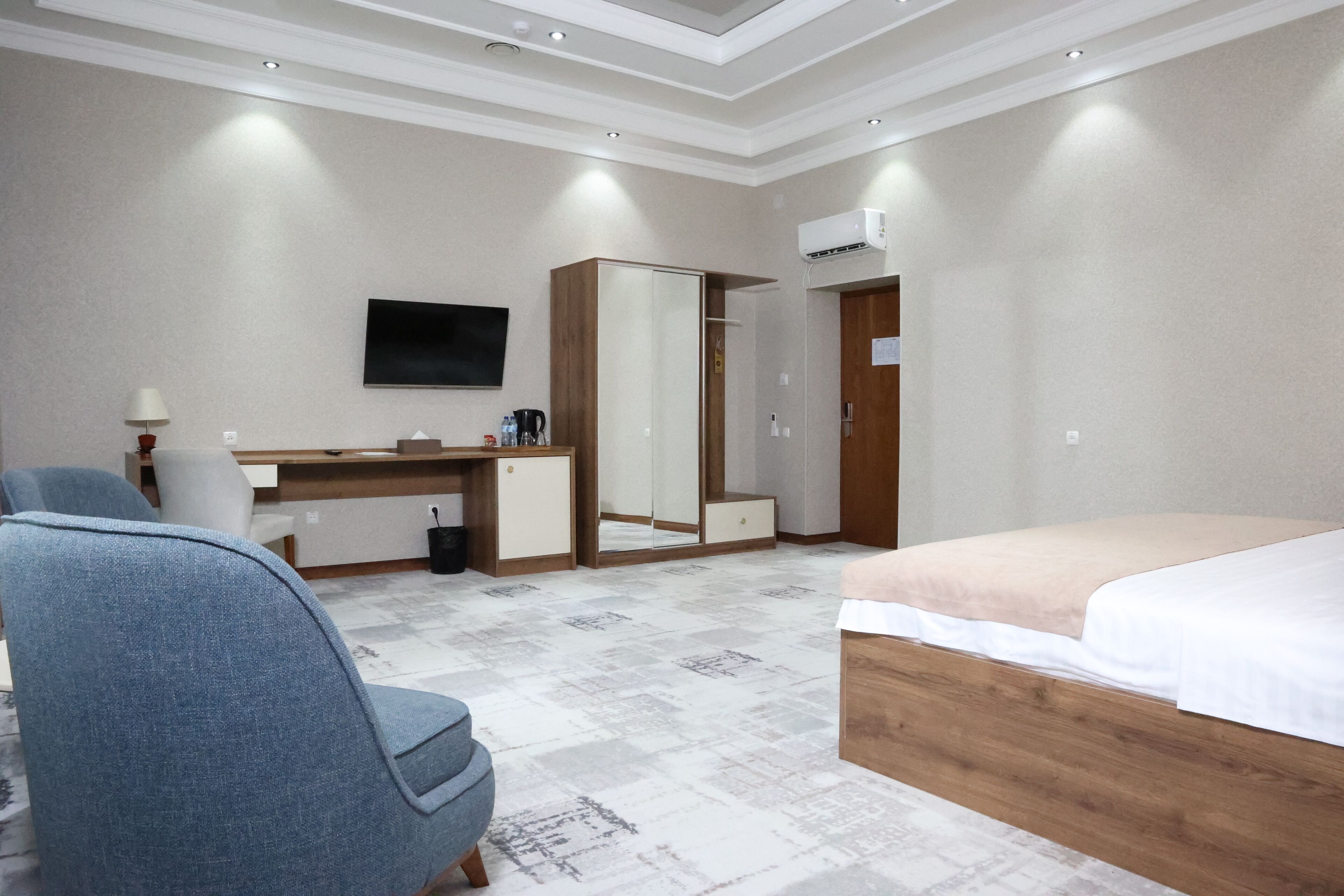 A hotel room with a bed, a desk, a chair, a wardrobe, a television, and an air conditioning unit.