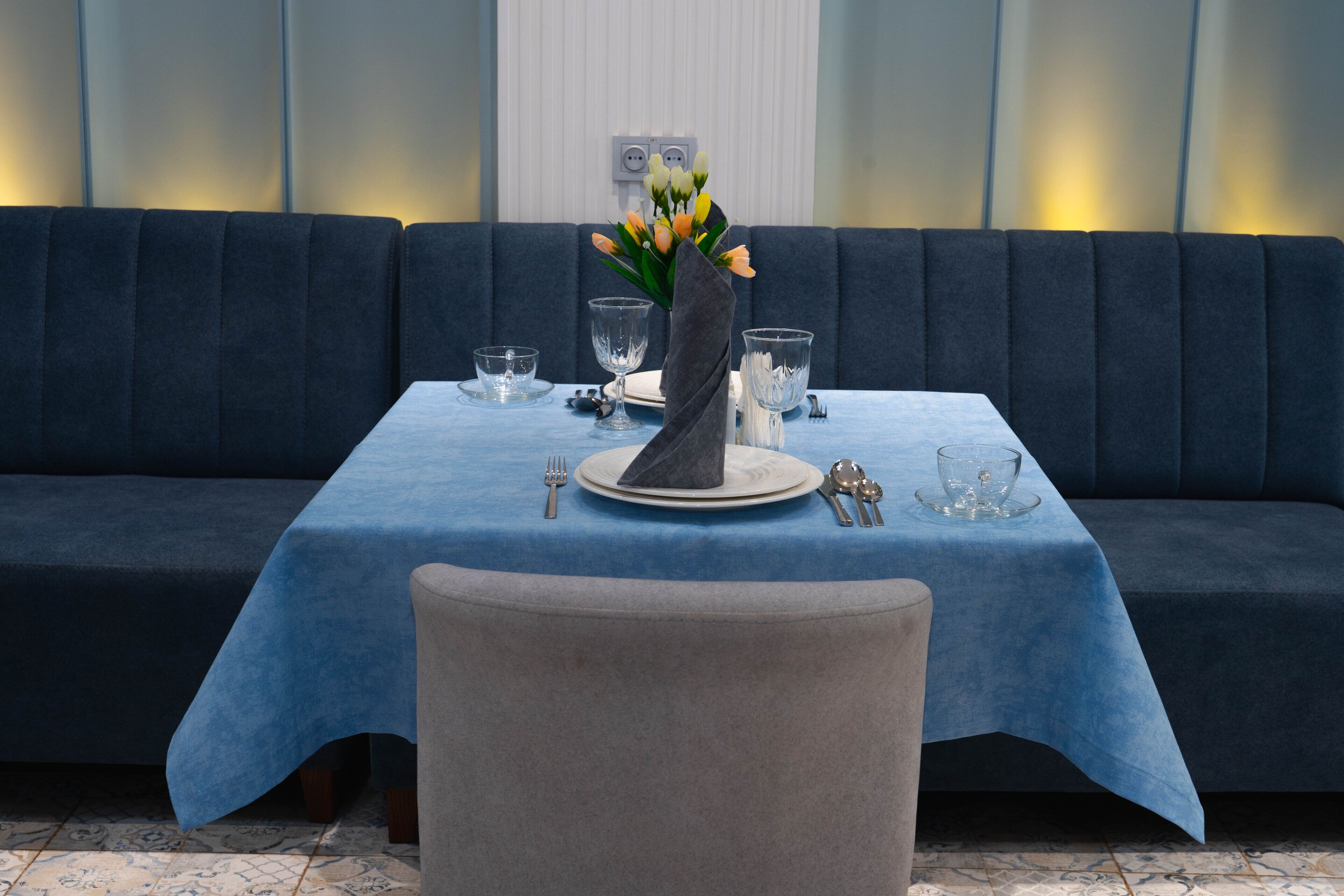 Un comedor con mantel azul, un jarrón de flores y una mesa impecablemente dispuesta con platos, vasos y cubiertos.