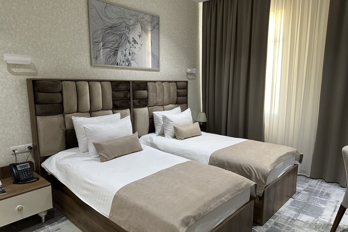 A hotel room with two beds, a headboard, a bedside table with a phone, and a painting on the wall.