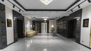 Una hall d'hotel moderna con pavimento in marmo, un lampadario, una poltrona e cartelli indicativi.
