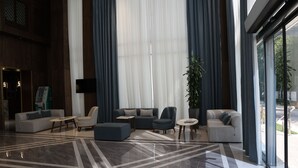 Un'ampia hall dall'arredamento moderno, con una vasta area salotto con divani e poltrone, pavimento decorato e grandi finestre con tende.
