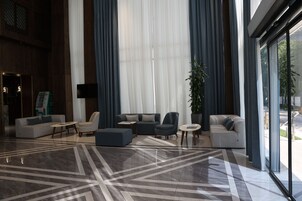 Tilava aula, jossa on moderni muotoilu. Aulassa on suuri oleskelualue, jossa on sohvia ja nojatuoleja, kuvioitu lattia sekä suuret ikkunat, joissa on verhot.