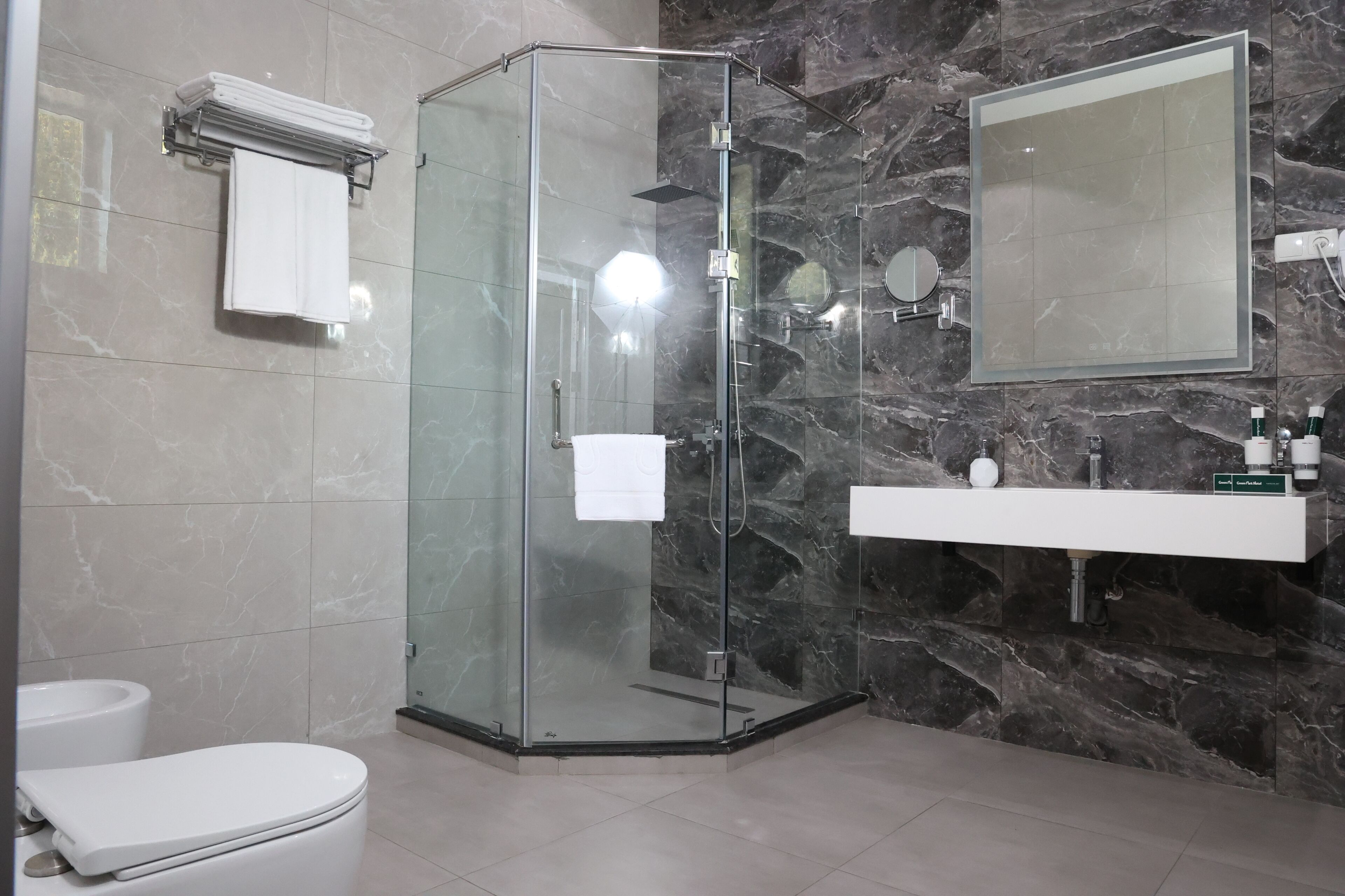 A modern bathroom with a glass-enclosed shower, a white toilet, a vanity with a mirror, and marble walls.