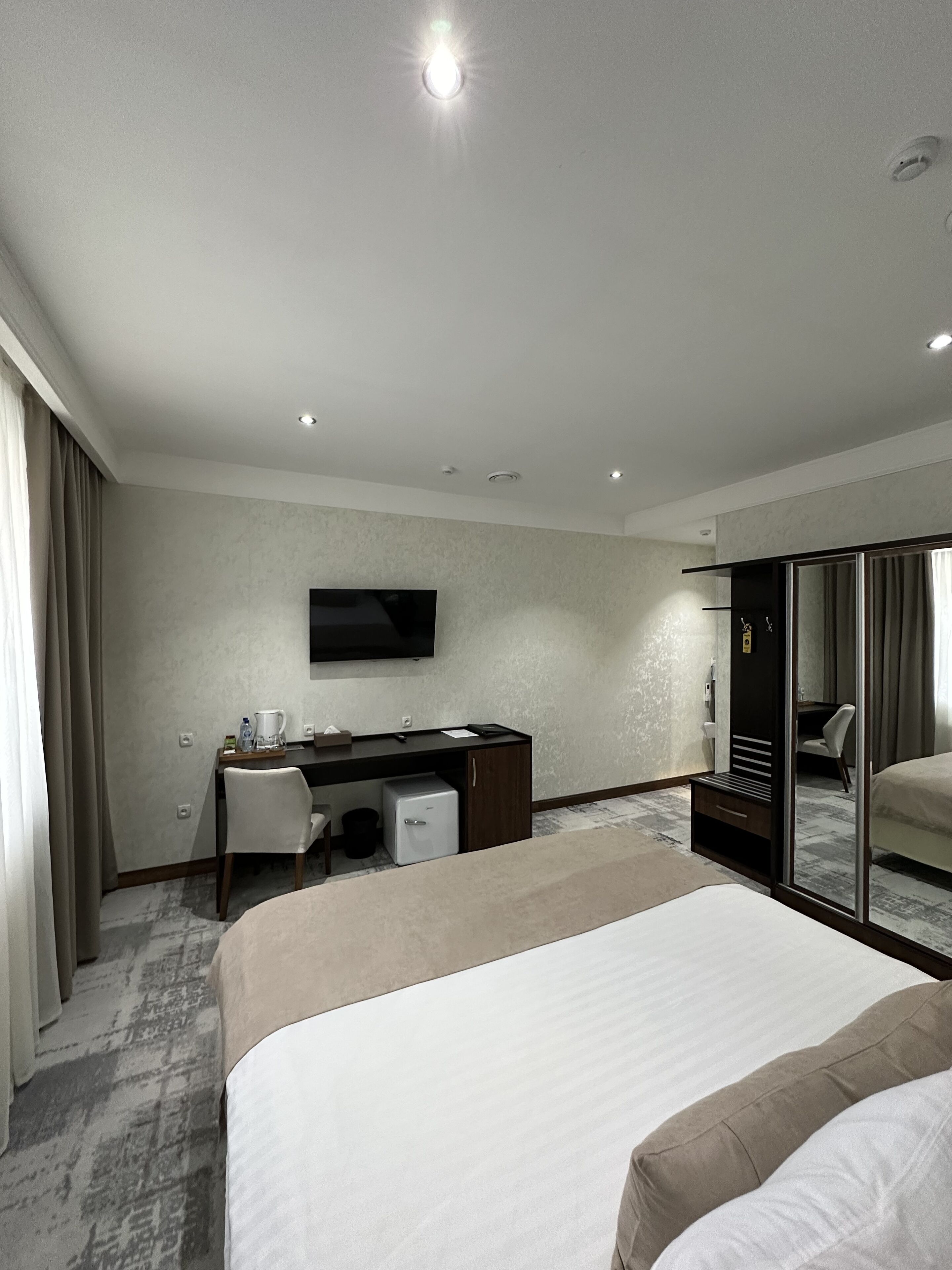 A hotel room with a bed, a desk with a chair, a television, and a wardrobe.