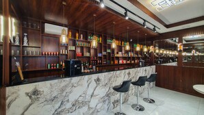 Angolo bar con bancone in marmo, numerose mensole piene di bevande e lampade pendenti.