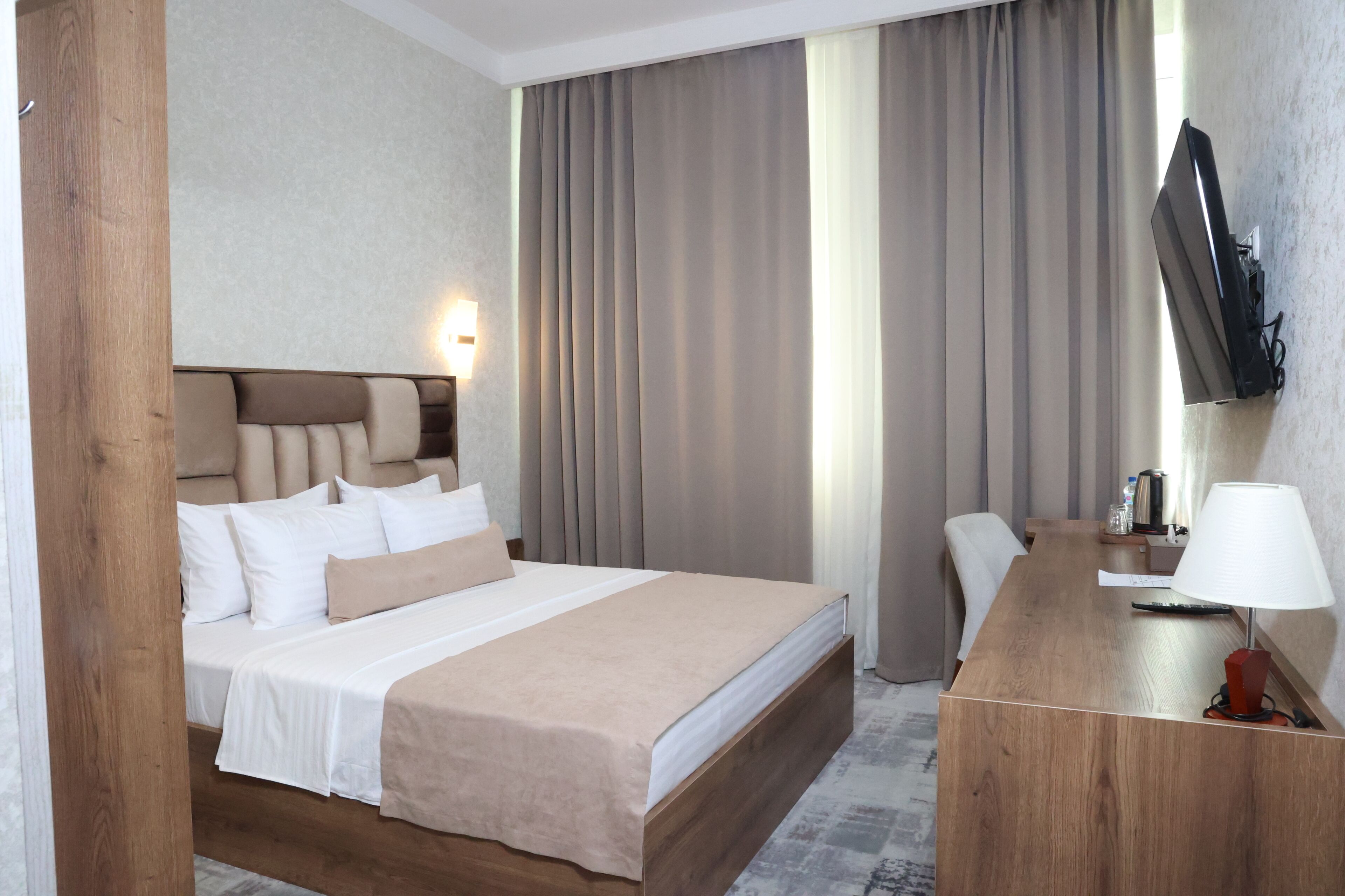 A hotel room with a bed, a desk, a chair, a television, and a lamp.