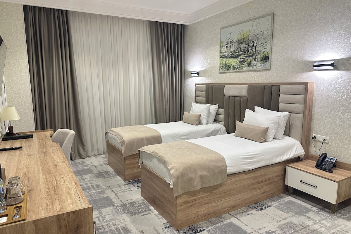 A hotel room with two beds, a desk, a chair, a nightstand with a phone, and a painting on the wall.