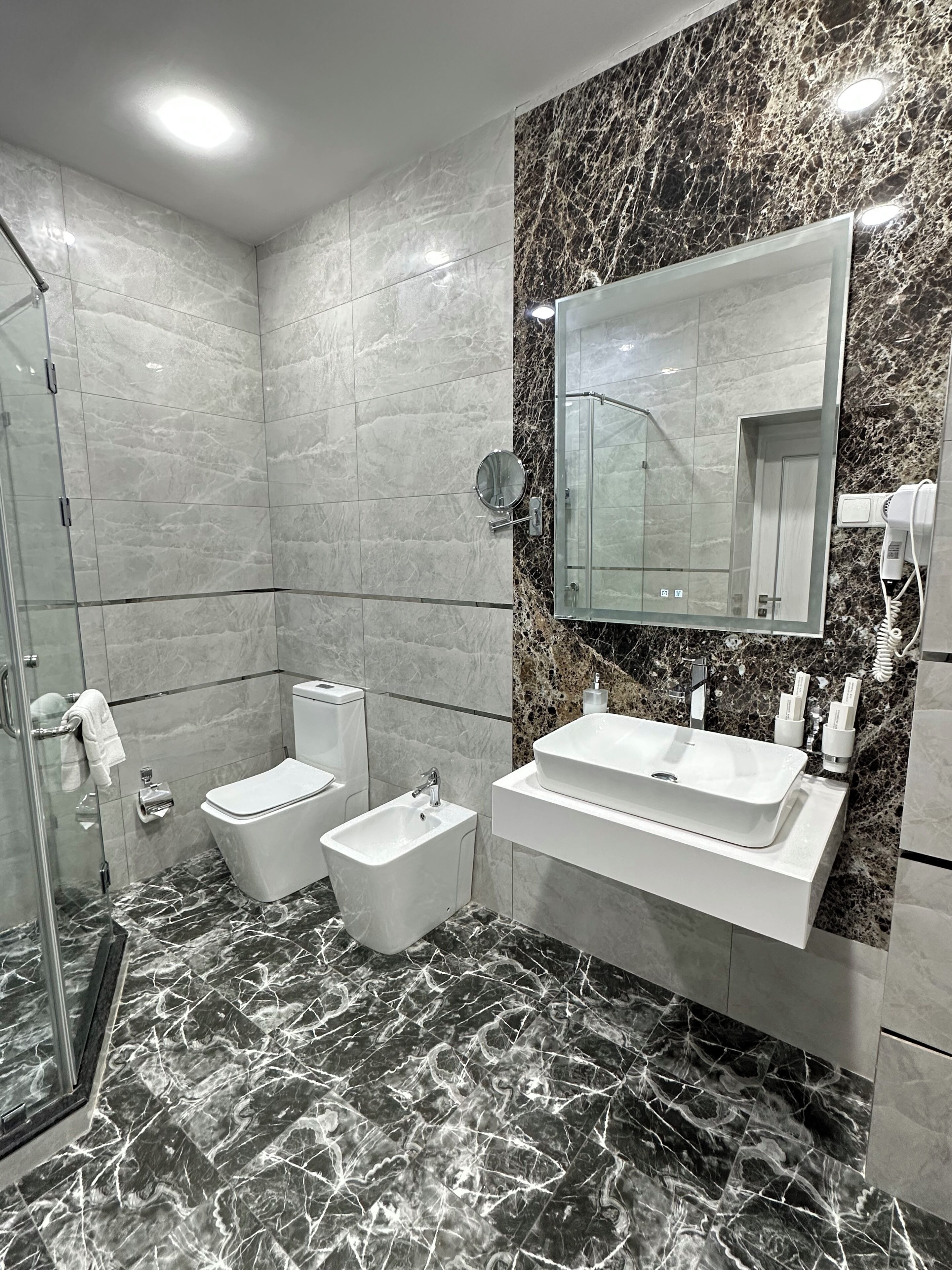 Un bany modern amb plat de dutxa de vidre, un vàter, un lavabo, un armari amb rentapans i un mirall gran.
