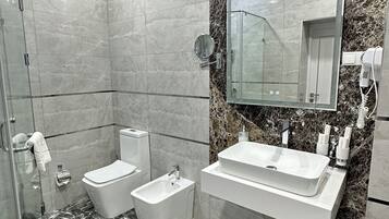 Un bany modern amb plat de dutxa de vidre, un vàter, un lavabo, un armari amb rentapans i un mirall gran.