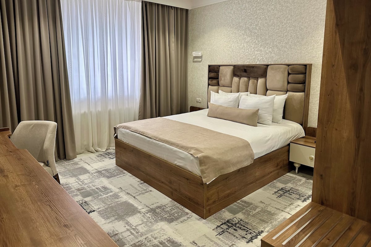 A hotel room with a wooden bed, beige bedding, a desk, and a chair.