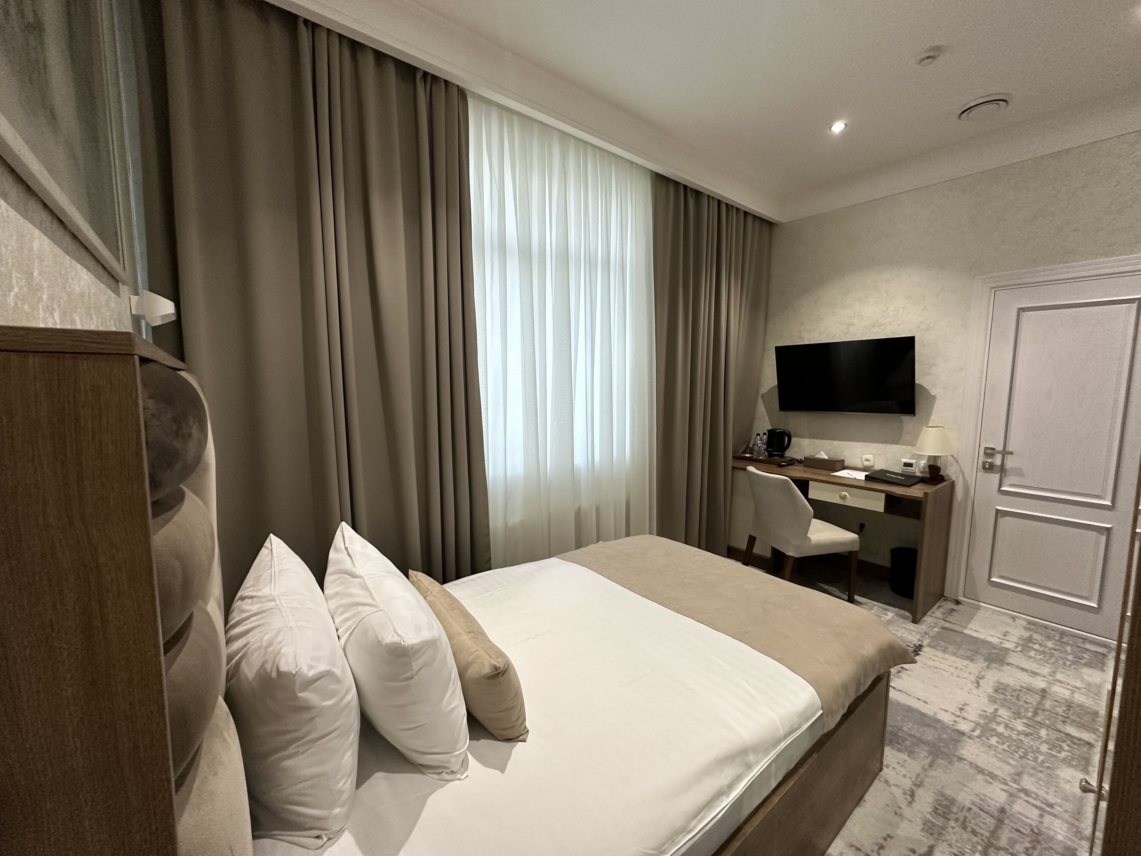 Ein Hotelzimmer mit Bett, Schreibtisch, Stuhl, Fernseher und einer Tür.