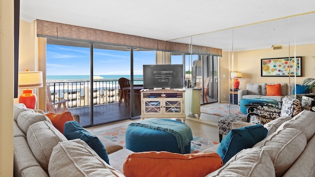 A modern living room with a large TV, comfortable seating, and a balcony with a view of the beach. - Ocean View, recently updated, 24 hour security + Free Attraction Tickets! (Myrtle Beach)