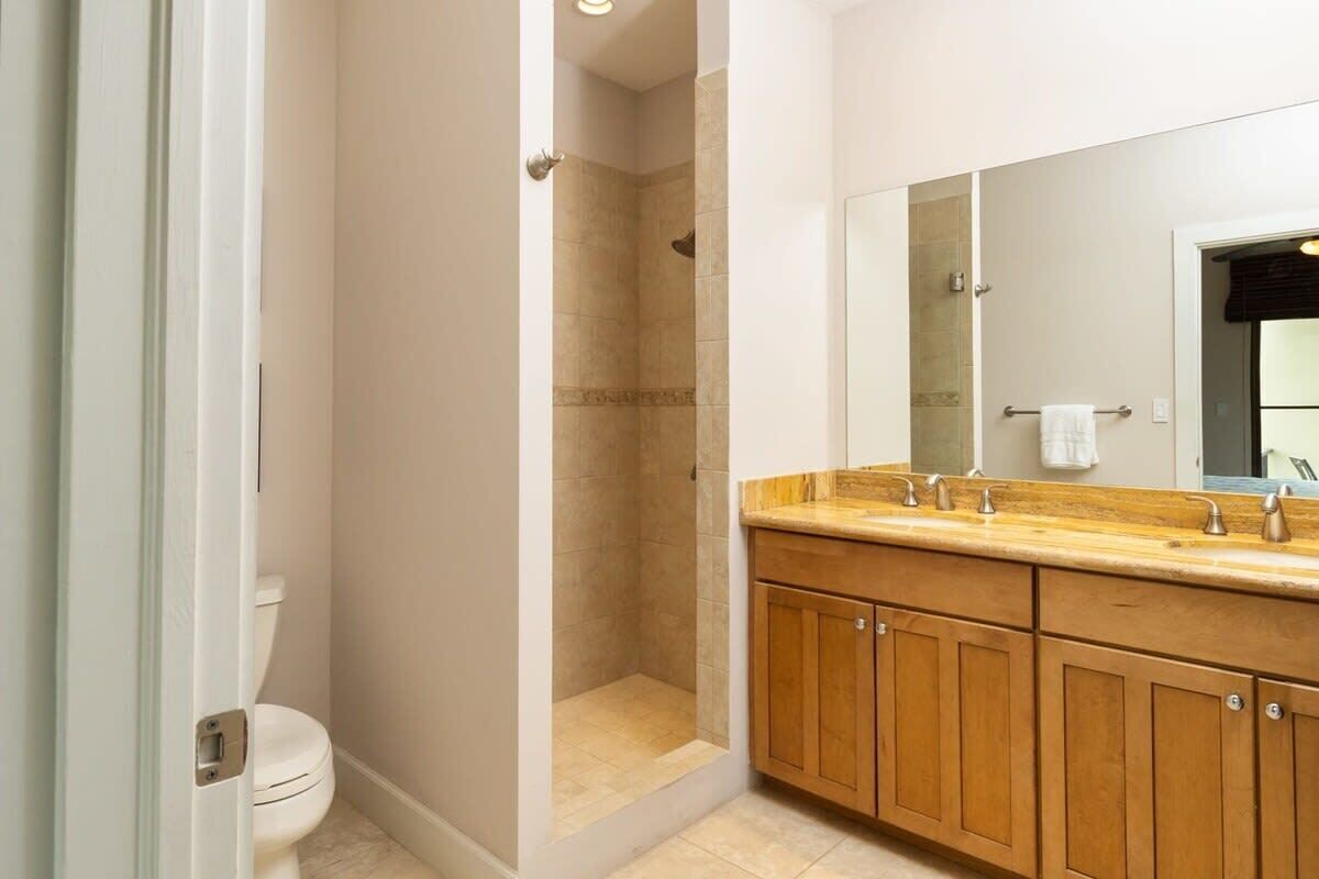 A bathroom with a shower, toilet, and wooden vanity with a mirror.