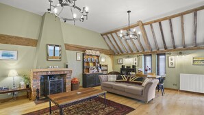 A spacious living room with a fireplace, wooden beams, a sofa, and a dining area.