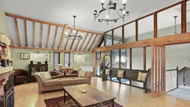 A spacious loft with exposed wooden beams, a large window, a wooden dining table, and a cozy seating area.