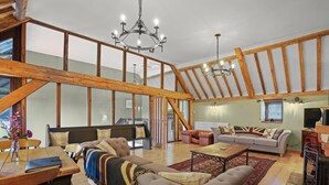A spacious loft-style living area with high ceilings, exposed wooden beams, and a large window.