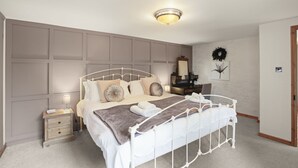 A bedroom with a white metal bed frame, a bedside table with drawers, a lamp, and a wall-mounted mirror.
