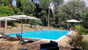 Une piscine rectangulaire dont le bord est recouvert de carreaux, entourée de chaises longues et de parasols.