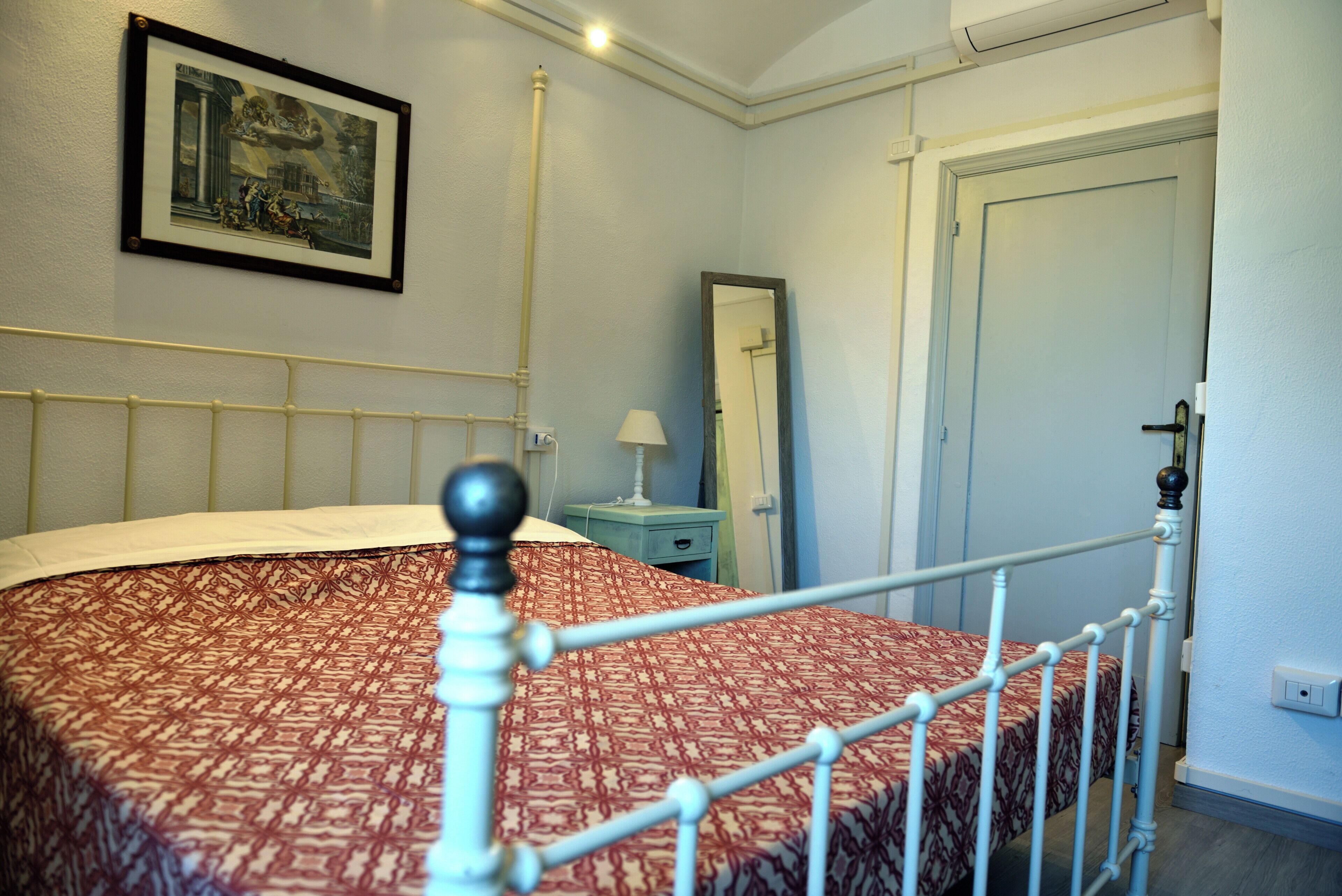 Una camera da letto con un letto, un comodino, una lampada, uno specchio e una porta.