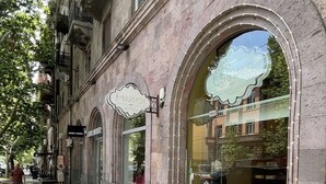 Una calle adoquinada con comercios, incluyendo una panadería con un amplio escaparate y un cartel que dice "MARIUSH".