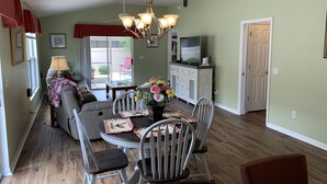 A dining area with a round table, chairs, a chandelier, and a television in the background. - Beautiful Dog Friendly Home with Gas Golf Cart, BBQ Grill, & FREE WiFi! (The Villages)