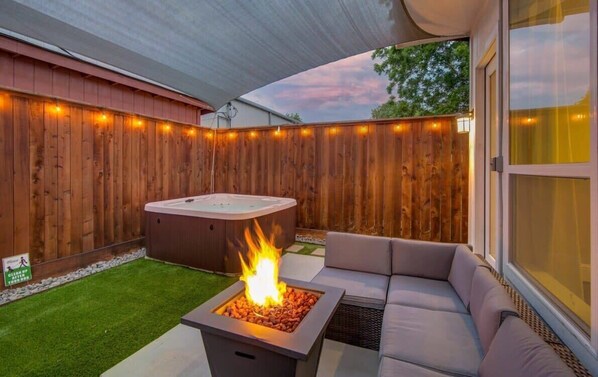 Relax in the backyard patio area with a fire feature, hot tub, and comfortable seating under a shaded canopy.
