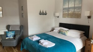 Une chambre à coucher comprenant un lit, une chaise, une table de chevet et un mur décoré d’œuvres d’art.