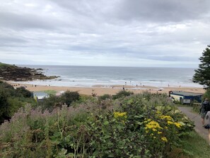Ein Strand mit Felsen, einem Sandufer und einem Weg zu einem Gebäude.