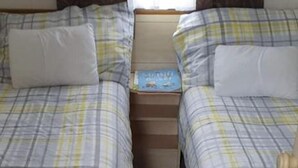A twin room with two beds, each with a plaid bedspread and white pillows. There is a small wooden nightstand between the beds with a book on it.